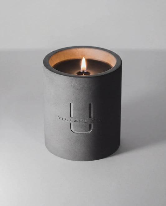 URU Candle in a black concrete holder with 'YOU ARE YOU' branding on a light gray background. Brutalist Concrete Candle